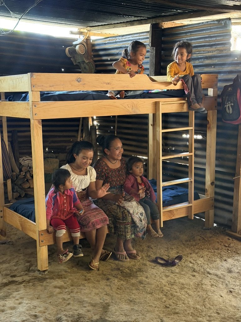 A family sitting on their new bunk bed in Yalú